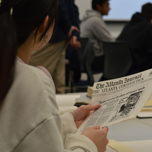 Student holding an archival newspaper at a research collective event by Declan Abernathy